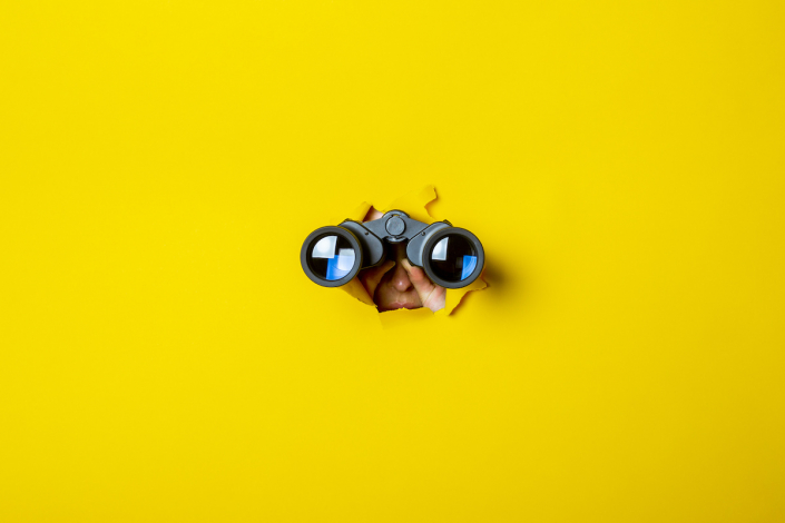 Female hand holds black binoculars on a yellow background. Journey, find and search concept